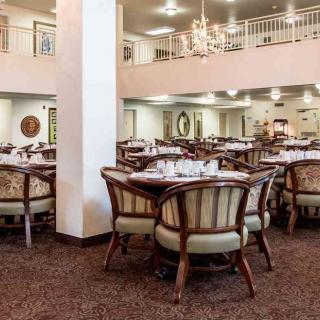 A spacious dining area with neatly arranged tables and chairs, featuring a chandelier and a carpeted floor.