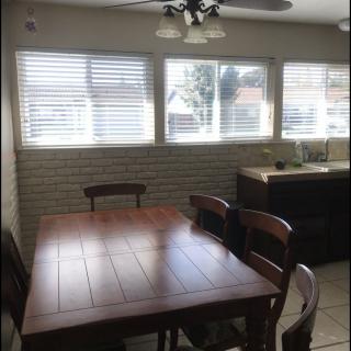 A cozy dining room with a wooden table set near large windows and blinds.