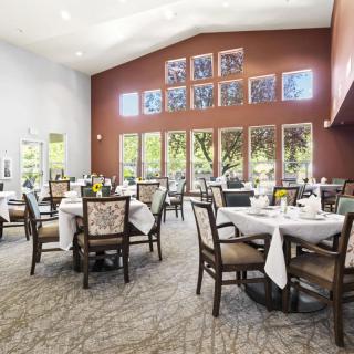 A well-lit dining room with elegantly set tables and large windows offering a view of the outdoors.