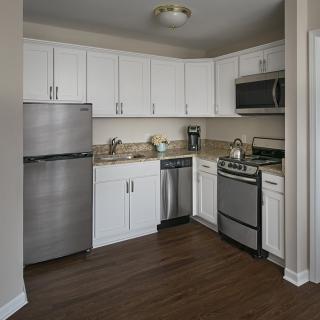 A modern kitchen with white cabinets, stainless steel appliances, and wood flooring.