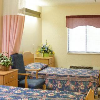 A hospital room with two beds, a chair, and a window with a curtain.