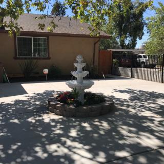 A sunny patio with a decorative fountain and surrounding trees casting shadows.