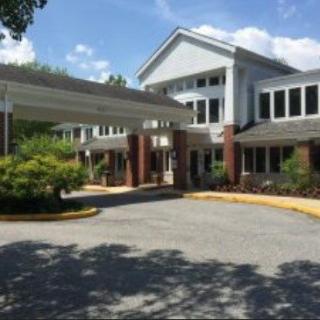 A large building with a covered entrance, surrounded by trees and a clear blue sky.