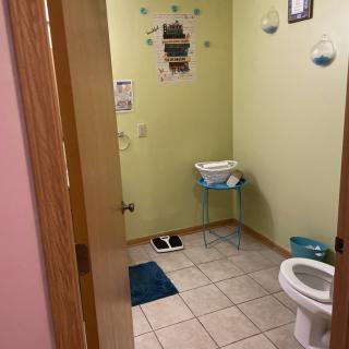 A small bathroom with green walls, featuring a toilet, tile flooring, and modern decor.