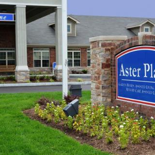 Exterior view of a building with a sign reading 'Aster Place' surrounded by landscaping.