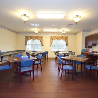 A cozy dining room setup with multiple tables and chairs, illuminated by ceiling lights and adorned with elegant curtains.