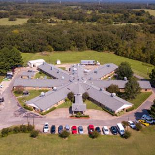 Aerial view of a unique building layout surrounded by lush greenery and a parking area.