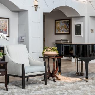 A luxurious lounge area featuring a grand piano, elegant furniture, and framed artwork on the walls.