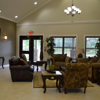 A cozy living room interior with sofas and chairs arranged around a coffee table, featuring large windows and decorative lighting.