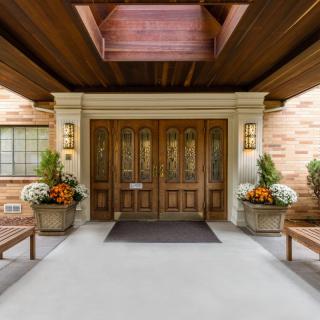 A welcoming entrance with wooden doors, decorated plants, and benches on either side under a wooden ceiling.