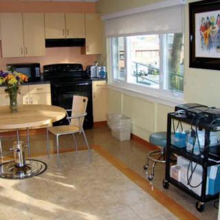 A cozy kitchen with a dining area featuring a round table, chairs, and a flower centerpiece. The room includes modern appliances and a utility cart by the window.