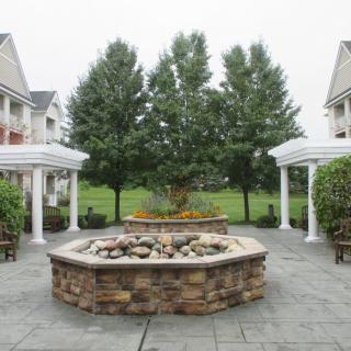 A scenic courtyard featuring a central stone fountain surrounded by lush greenery and pillars.