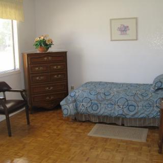 A simple bedroom with a single bed, dresser, and chair by the window.