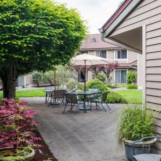 A serene outdoor space featuring a patio with seating, surrounded by vibrant greenery and flowers.