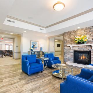 A modern living room with blue chairs, a stone fireplace, and wood flooring.