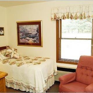 A cozy bedroom with a single bed, an armchair, and wall decorations by a window.
