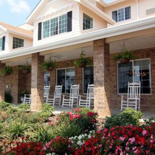 A charming building with a porch featuring rocking chairs, surrounded by colorful flowers and greenery.