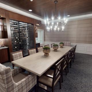 A modern dining room featuring a long table with chairs, a prominent wine rack, and stylish lighting.