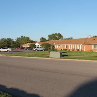 A view of a quiet residential area with neatly arranged buildings and parked cars under a clear blue sky.