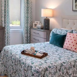 A cozy bedroom with patterned bedding, accent pillows, and a bedside lamp.