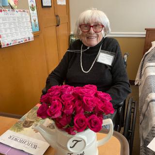An elderly woman in a wheelchair enjoys a vibrant bouquet of roses in a care facility.