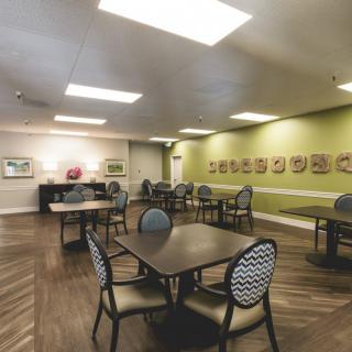 A well-lit dining area with neatly arranged tables and chairs, complemented by artwork on the walls.