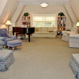 A spacious living room with a grand piano, comfortable seating, bookshelves, and large windows.