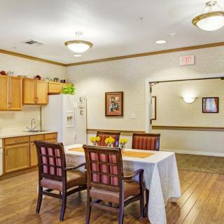 A well-lit dining area with a wooden table and chairs, adjacent to a kitchen space.