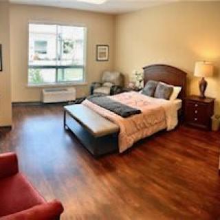 A cozy bedroom with a large bed, hardwood floors, and natural light from a window.