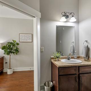 A modern bathroom with a vanity and mirror, connected to a bedroom featuring contemporary decor and a houseplant.