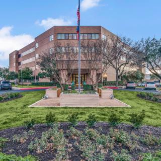 A large office building with a landscaped garden and flagpole in front.