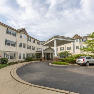 A view of a multi-story building with a driveway and parking area at the entrance.