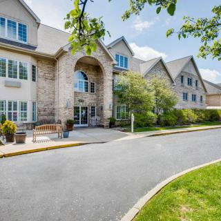 A large building with a welcoming entrance, surrounded by well-maintained landscaping and trees on a sunny day.
