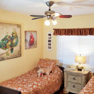 A cozy bedroom with twin beds, bird-themed artwork, and a ceiling fan.