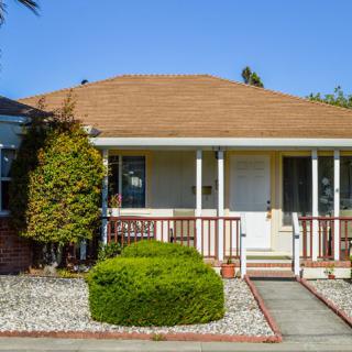 A cozy bungalow with a front porch and landscaped garden on a sunny day.