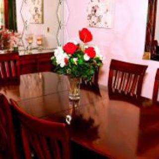 A dining room with a wooden table and chairs, decorated with a vase of red and white flowers.