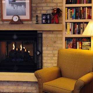 A cozy living room with a fireplace, armchair, and a well-stocked bookshelf.