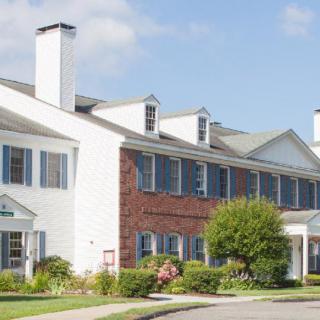A suburban residential building with a combination of brick and white siding, featuring multiple windows and chimneys.