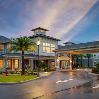 An elegant hotel with modern architecture, illuminated in the evening, surrounded by palm trees.