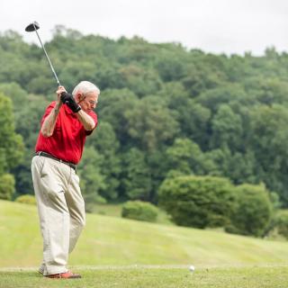 A senior golfer swinging a club on a lush green course.