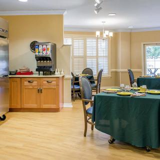 A well-lit dining room with neatly set tables and a kitchen area.