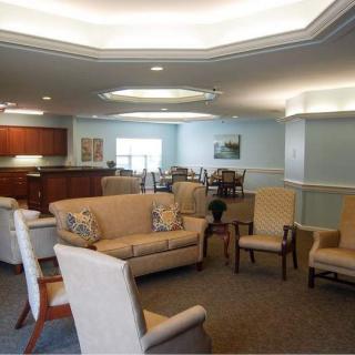 A comfortable living room with sofas and chairs arranged around a central table, featuring elegant lighting.