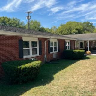 A brick residential house with a grassy yard and bushes under a sunny sky.