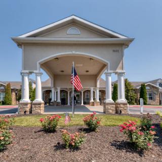 A grand building entrance with columns and an American flag, surrounded by landscaped flowers.