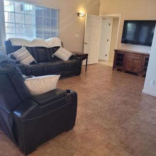 A cozy living room featuring a black leather sofa, an armchair, and a television.