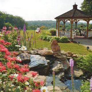 A picturesque garden with vibrant flowers and a tranquil pond, featuring a wooden gazebo in the background.