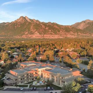 An aerial view of a residential area surrounded by lush trees with a backdrop of mountains during sunset.