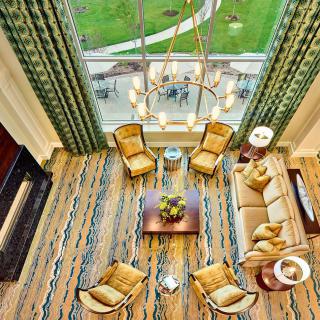 A beautifully designed living room with a cozy seating arrangement, seen from an aerial perspective. The room features a stylish chandelier, large windows, and modern furniture.