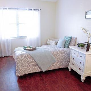 A cozy and well-lit bedroom featuring a bed with patterned bedding and a white nightstand.