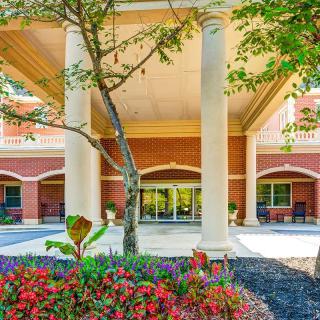 The entrance of a building with columns and landscaped flowers and trees.